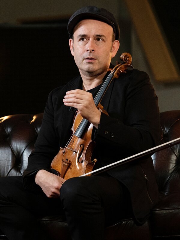Aleksey Igudesman sits on a sofa holding his violin. Photo by Larissa Matheus.