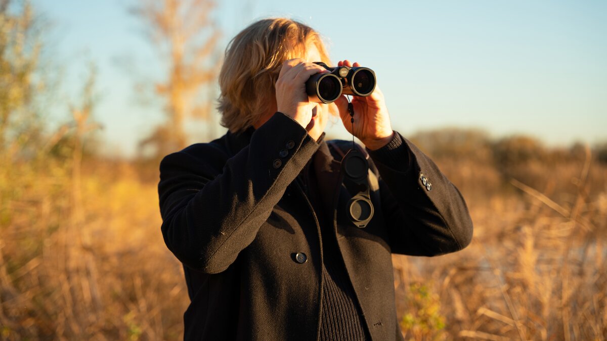 Dominik Eulberg out in a grassy field looking through binoculars.