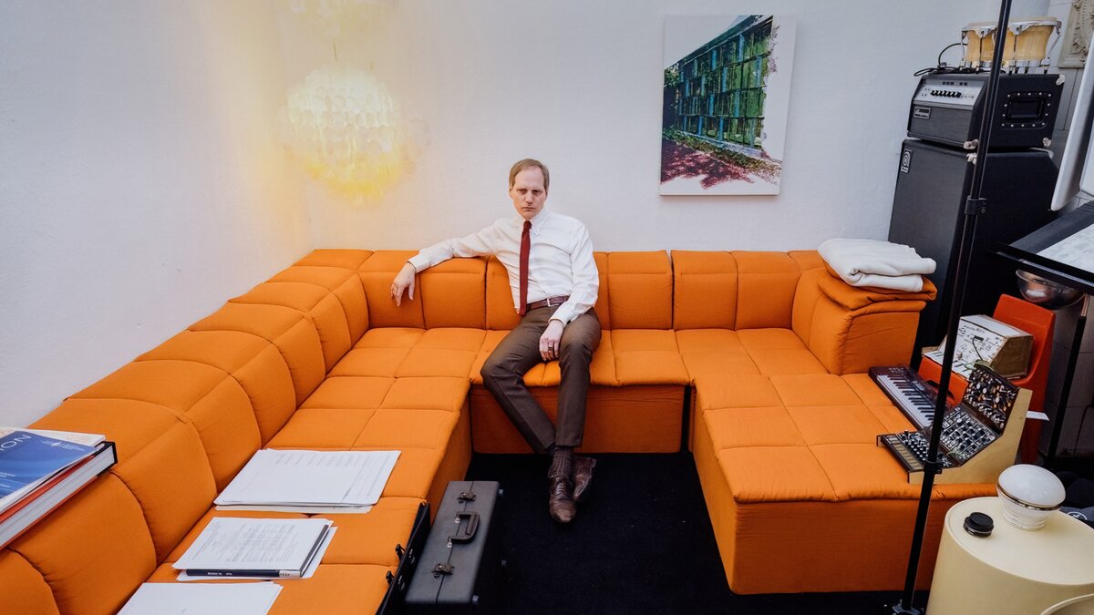 Max Knoth in a suit on an orange couch in his studio