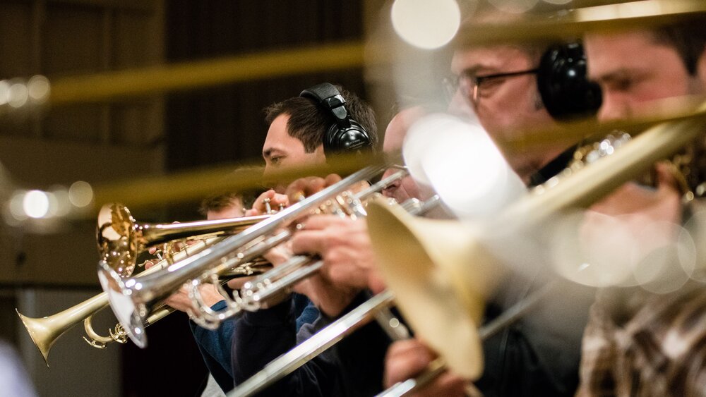 A row of trumpet and trombone players during a sample library recording session