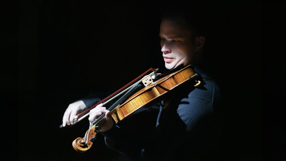 A man playing a viola in high-contrast lighting