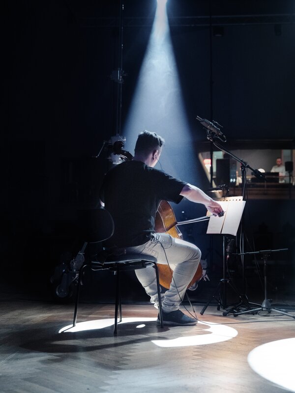 A cello player in a spotlight at a recording session