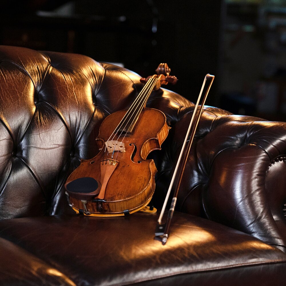A violin on a leather sofa. Photo by Larissa Matheus.